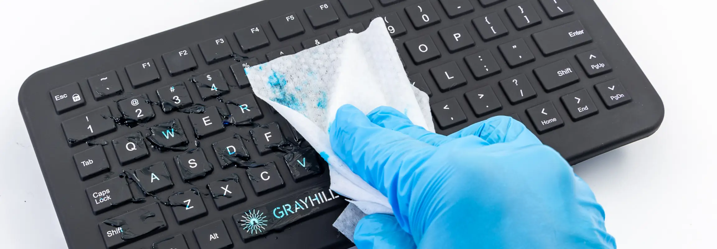 Blue glove wiping up ultrasound gel on a Black Grayhill Medical Keyboard with a cleaning wipe.
