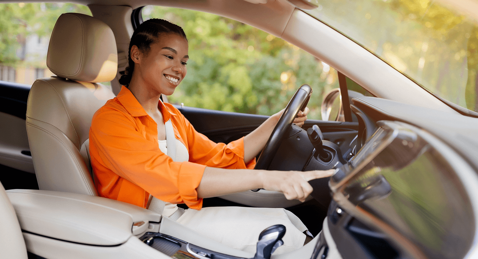 A woman smiles in the driver's seat of a car while pressing a pushbutton control on the infotainment center on the dashboard.